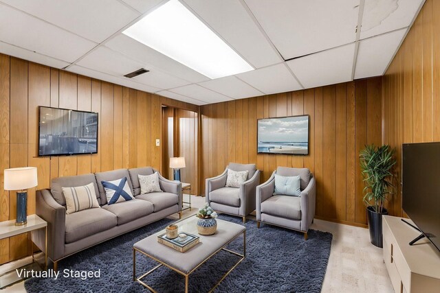 living room featuring a paneled ceiling and wooden walls