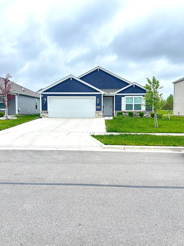 ranch-style house featuring an attached garage, driveway, a front lawn, and stone siding