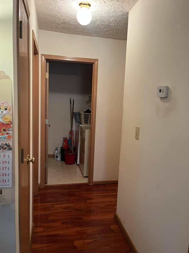 hallway with wood finished floors, a textured ceiling, separate washer and dryer, and baseboards