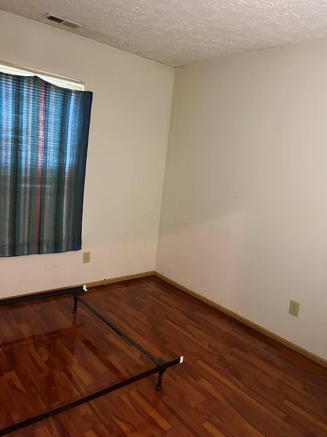 empty room with a textured ceiling, wood finished floors, and baseboards
