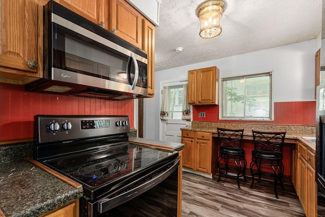 2584 E 5th Ave, Columbus, OH 43219 - kitchen with range with electric stovetop, stainless steel microwave, light wood finished floors, a textured ceiling, and brown cabinets