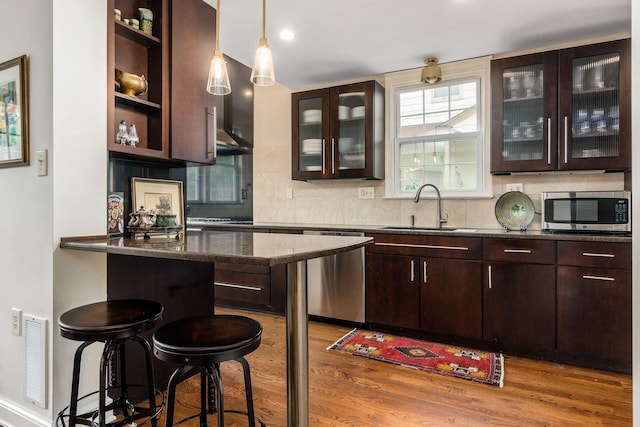 bar area featuring a sink, appliances with stainless steel finishes, wood finished floors, decorative backsplash, and hanging light fixtures