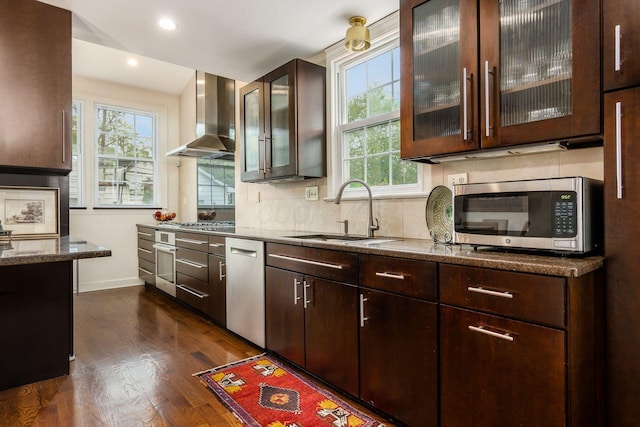 kitchen with appliances with stainless steel finishes, wall chimney exhaust hood, a sink, dark brown cabinets, and recessed lighting