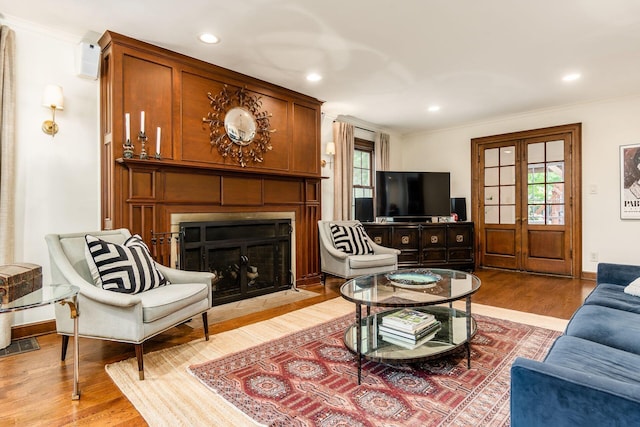 living room featuring light wood-style floors, healthy amount of natural light, a fireplace with flush hearth, ornamental molding, and recessed lighting