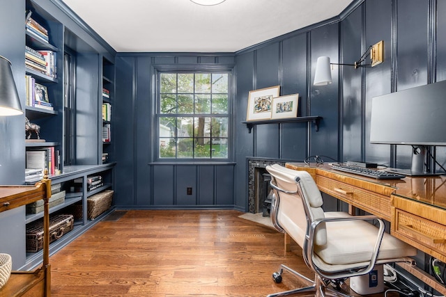 office space with a decorative wall, wood finished floors, built in shelves, and crown molding