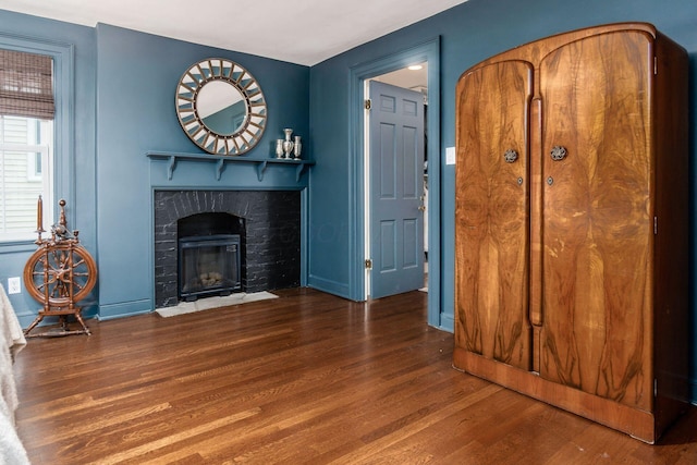 unfurnished living room featuring wood finished floors, a brick fireplace, and baseboards