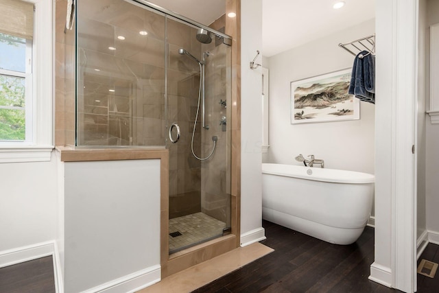 bathroom featuring wood finished floors, a shower stall, a soaking tub, baseboards, and recessed lighting