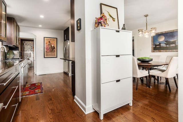 kitchen featuring a sink, dark brown cabinets, dark wood finished floors, a chandelier, and freestanding refrigerator