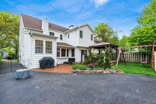 rear view of property with a gazebo, a chimney, a patio, and roof with shingles