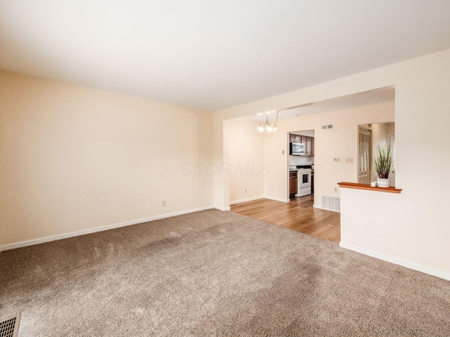 unfurnished living room featuring carpet floors, a chandelier, and baseboards