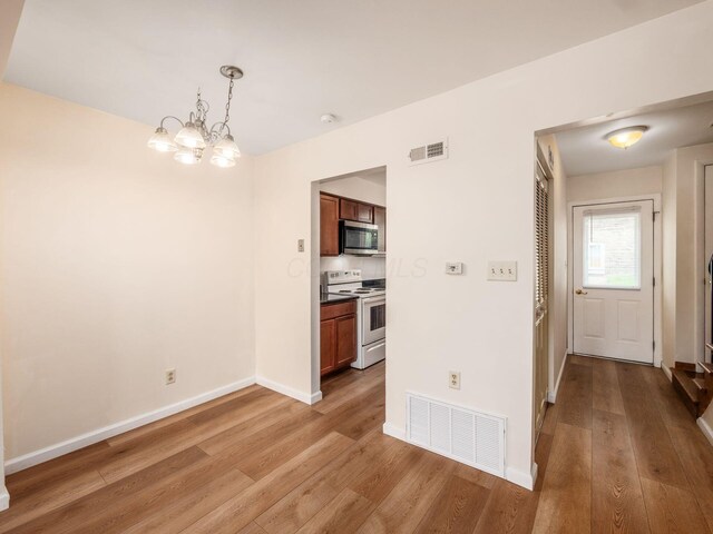 kitchen with electric stove, stainless steel microwave, wood finished floors, a chandelier, and baseboards