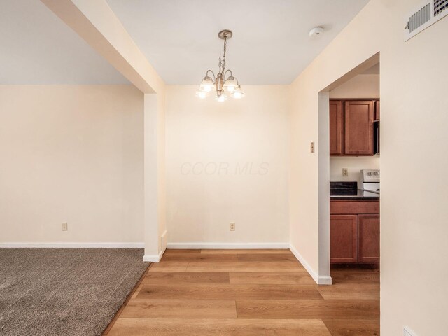 unfurnished dining area featuring a chandelier, light wood-style flooring, and baseboards