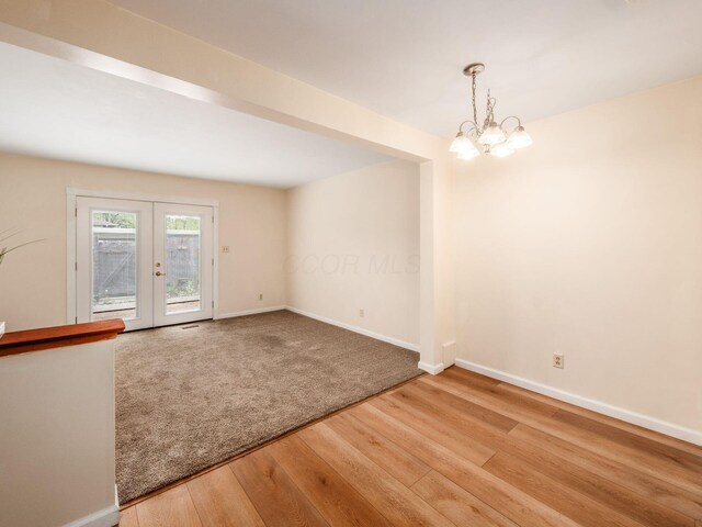 unfurnished dining area with wood finished floors, baseboards, a chandelier, and french doors