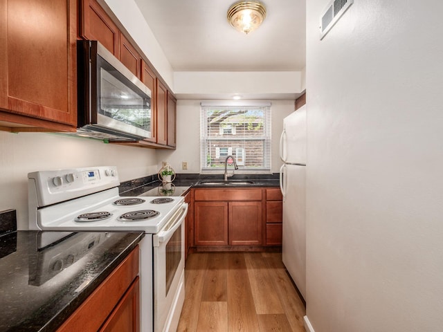 kitchen featuring white appliances, a sink, light wood-type flooring, brown cabinets, and dark stone counters