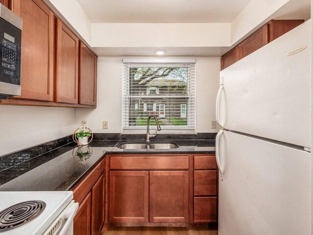 kitchen featuring freestanding refrigerator, a sink, dark stone countertops, and brown cabinetry