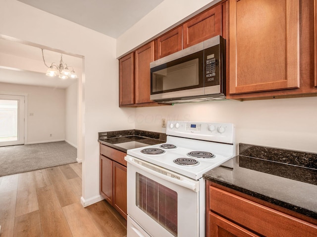 kitchen featuring stainless steel microwave, white range with electric cooktop, brown cabinets, light wood-style floors, and dark stone countertops