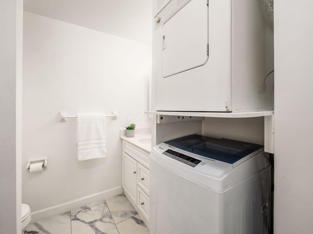 washroom featuring stacked washer and clothes dryer, baseboards, and light marble finish flooring