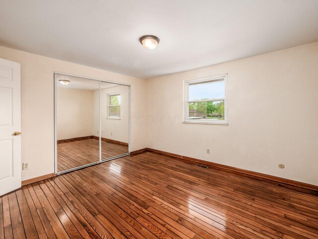 unfurnished bedroom featuring wood-type flooring, multiple windows, baseboards, and a closet