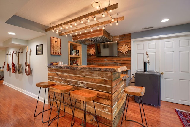 bar with baseboards, indoor bar, visible vents, and wood finished floors