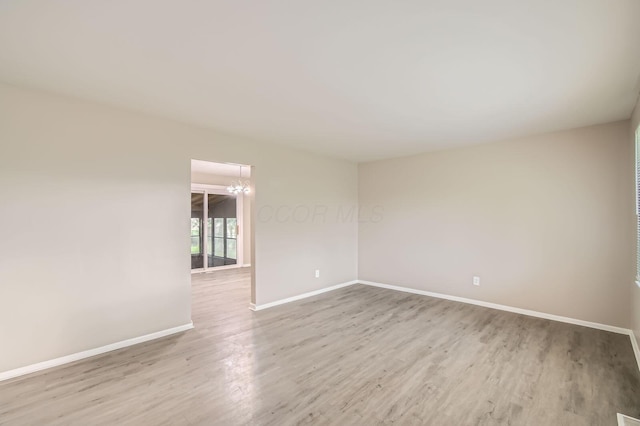 unfurnished room featuring wood finished floors, baseboards, and a chandelier