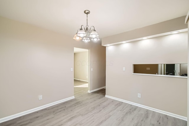 empty room featuring light wood-style floors, a chandelier, and baseboards