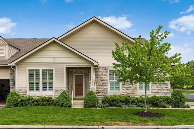 view of front facade with stone siding, a front lawn, and a shingled roof