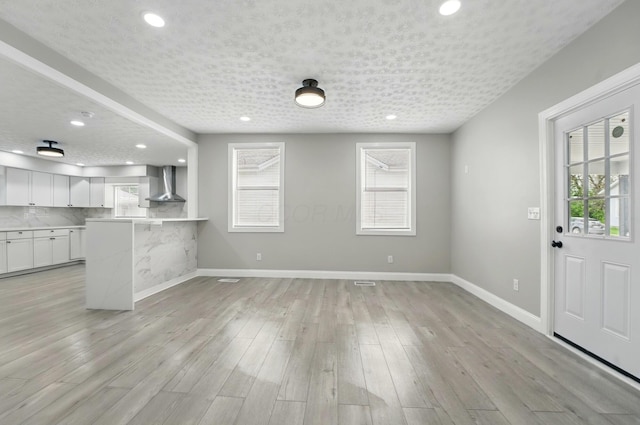 kitchen with baseboards, wall chimney range hood, white cabinets, and recessed lighting