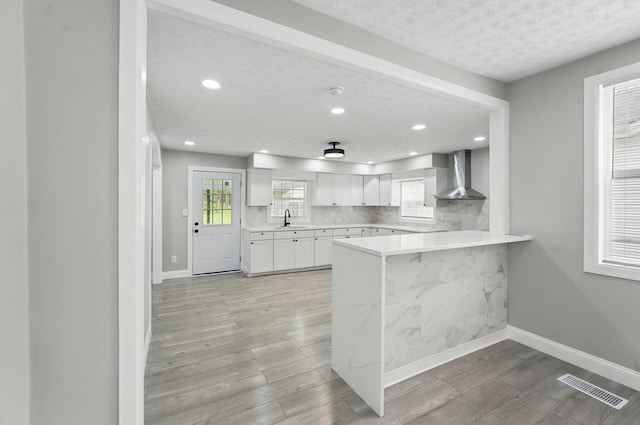 kitchen with a sink, wall chimney exhaust hood, light wood-type flooring, visible vents, and light countertops