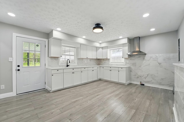kitchen with wall chimney range hood, light countertops, a healthy amount of sunlight, and a sink