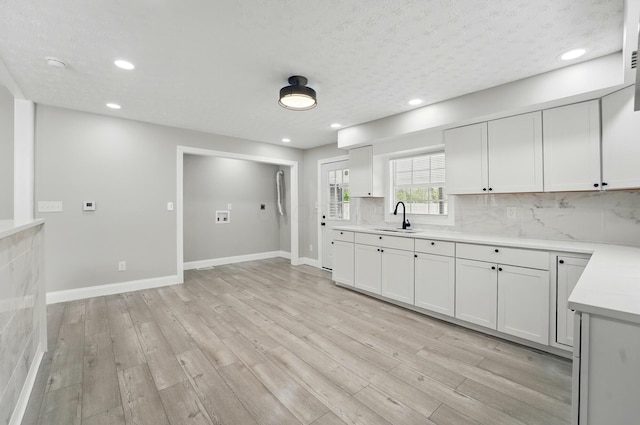 kitchen with a sink, light wood-style flooring, light countertops, and decorative backsplash