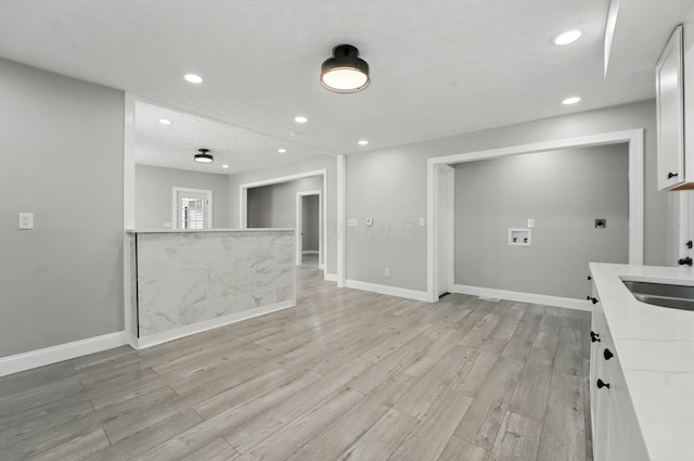 kitchen featuring light wood-style flooring, recessed lighting, baseboards, a sink, and white cabinets