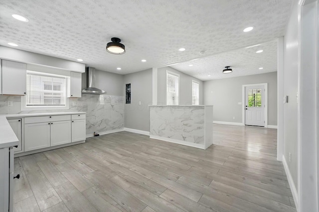 kitchen featuring wall chimney range hood, light wood-style floors, light countertops, and baseboards