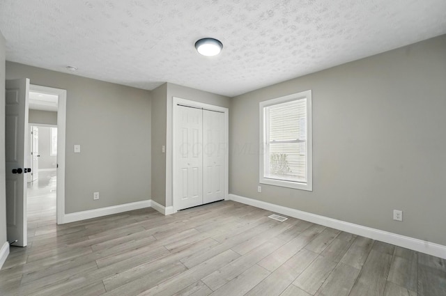 unfurnished bedroom featuring light wood-style flooring, baseboards, a closet, and visible vents