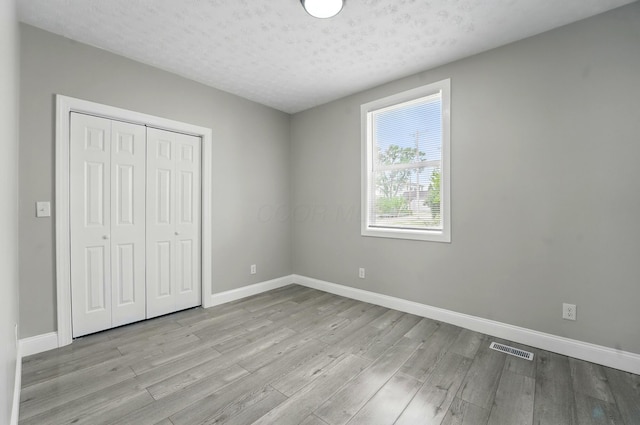 unfurnished bedroom with a closet, visible vents, wood finished floors, and baseboards