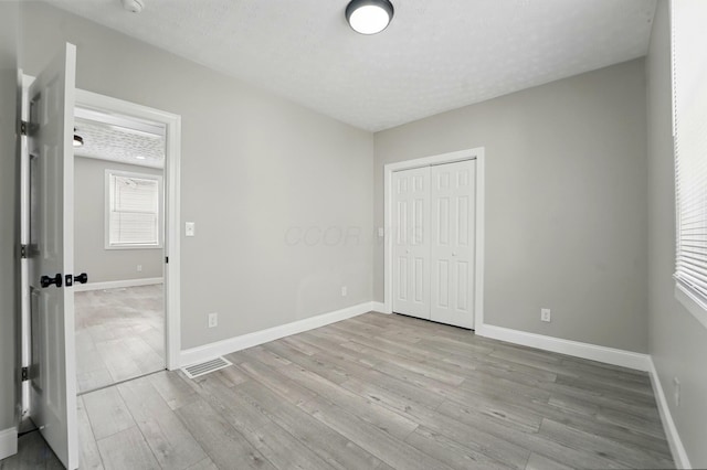 unfurnished bedroom with light wood finished floors, a closet, visible vents, and baseboards
