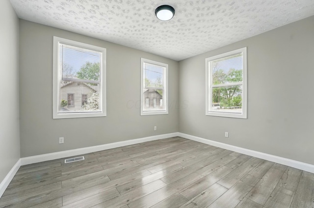 spare room with wood finished floors, visible vents, baseboards, and a textured ceiling