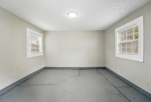 unfurnished room with concrete flooring, baseboards, and plenty of natural light