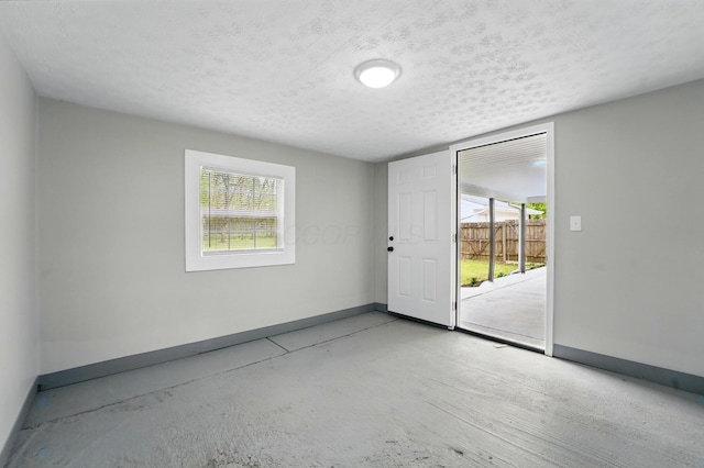 spare room with concrete floors, a textured ceiling, and baseboards