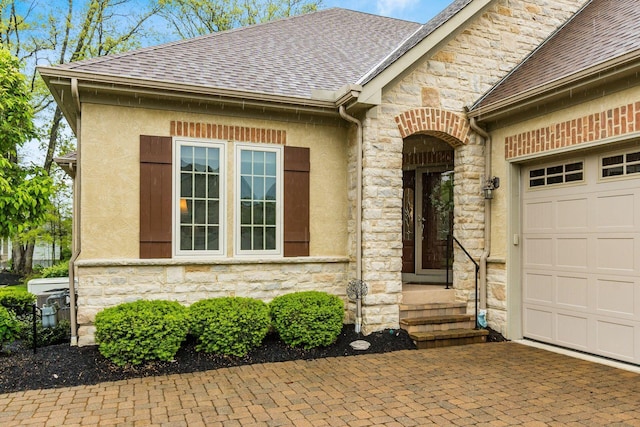 5464 Slater Rdg, Westerville, OH 43082 - view of exterior entry with stone siding, a garage, roof with shingles, stucco siding, and decorative driveway