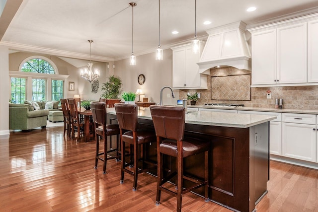5464 Slater Rdg, Westerville, OH 43082 - kitchen featuring custom exhaust hood, stainless steel gas stovetop, decorative backsplash, an island with sink, and wood finished floors