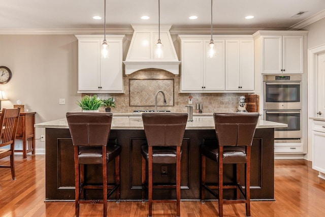 5464 Slater Rdg, Westerville, OH 43082 - kitchen featuring double oven, premium range hood, a kitchen island with sink, wood finished floors, and backsplash