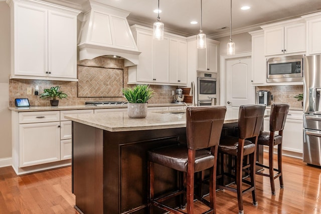 5464 Slater Rdg, Westerville, OH 43082 - kitchen featuring premium range hood, appliances with stainless steel finishes, a breakfast bar, light wood-style floors, and a center island with sink