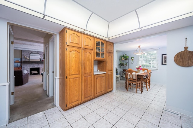 1211 Darcann Dr, Columbus, OH 43220 - kitchen featuring light tile patterned flooring, brown cabinetry, a brick fireplace, baseboards, and glass insert cabinets