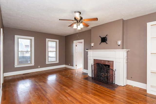 unfurnished living room with wood finished floors, baseboards, ceiling fan, a brick fireplace, and a textured ceiling