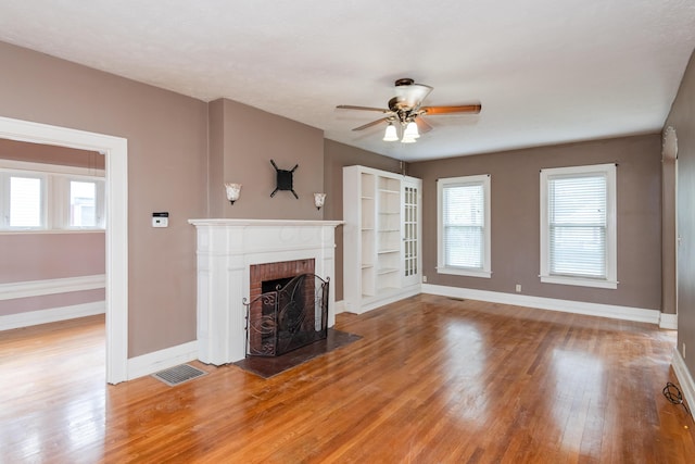 unfurnished living room featuring a brick fireplace, light wood-type flooring, baseboards, a ceiling fan, and healthy amount of natural light