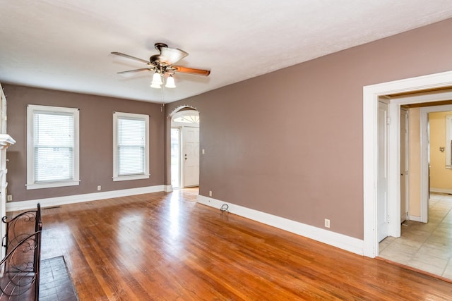 unfurnished living room featuring ceiling fan, light wood-type flooring, baseboards, and arched walkways