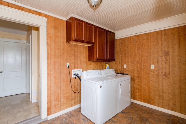 clothes washing area with cabinet space, baseboards, washing machine and clothes dryer, and wooden walls