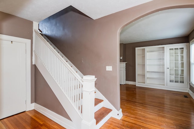 staircase with arched walkways, wood finished floors, and baseboards