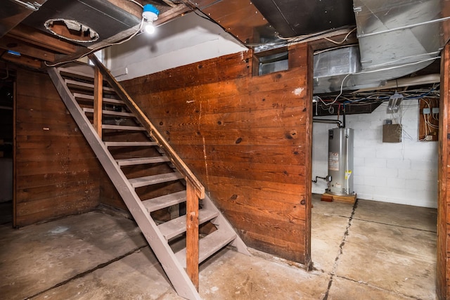 unfinished below grade area featuring water heater, stairway, concrete block wall, and wooden walls