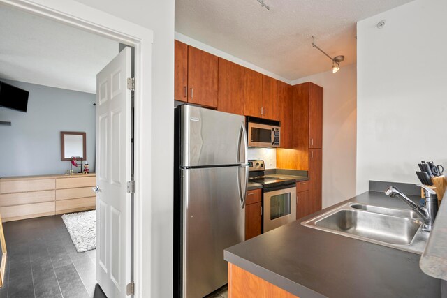kitchen with appliances with stainless steel finishes, a sink, brown cabinets, and dark countertops